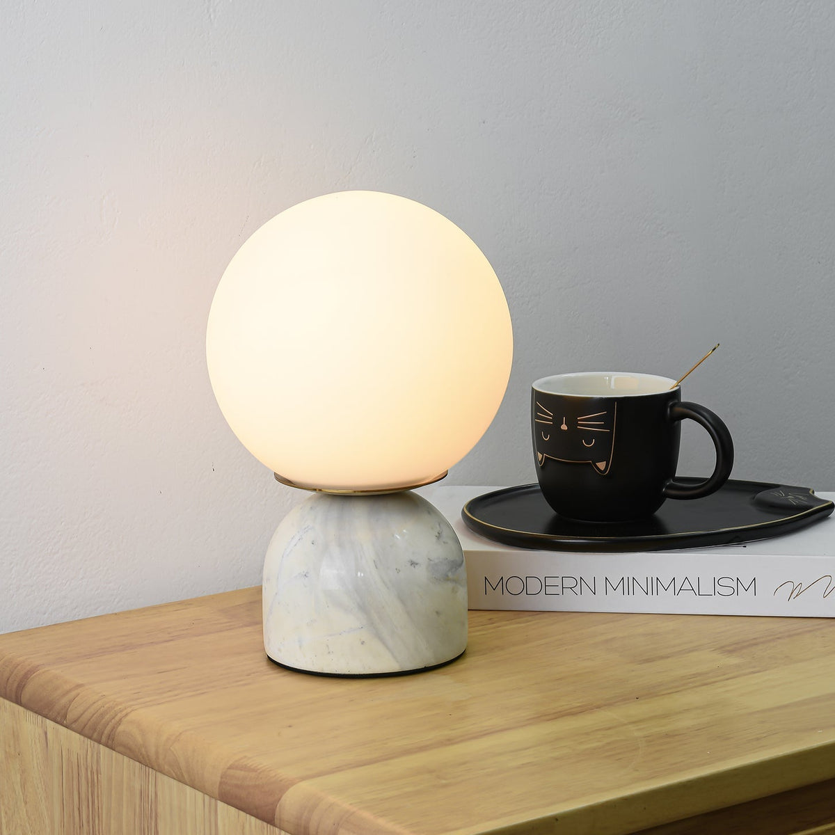 Lámpara de mesita Dunela con globo opal y base de mármol sobre una mesa de madera – imagen 3