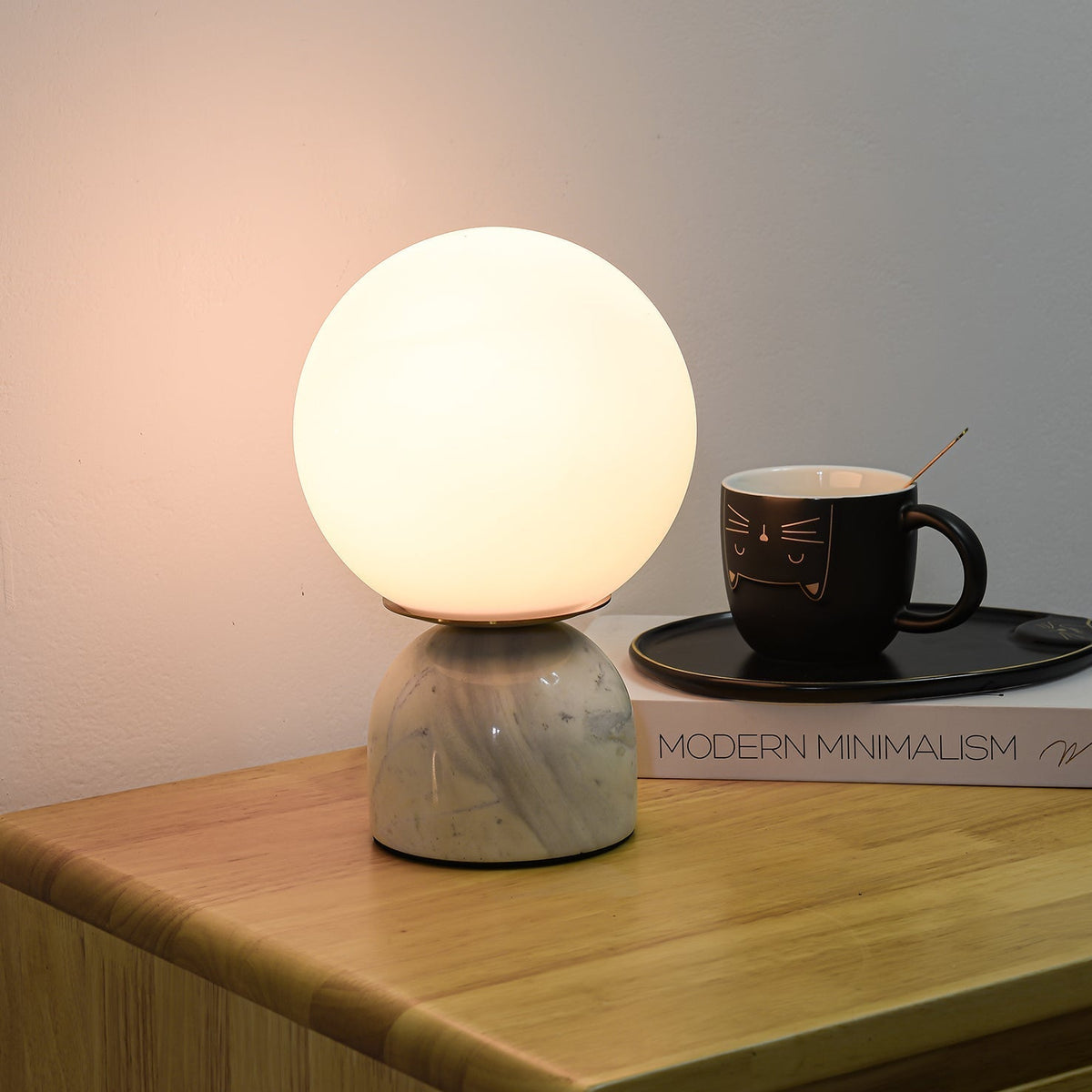 Lámpara de mesita Dunela con globo opal y base de mármol sobre una mesa de madera – imagen 4