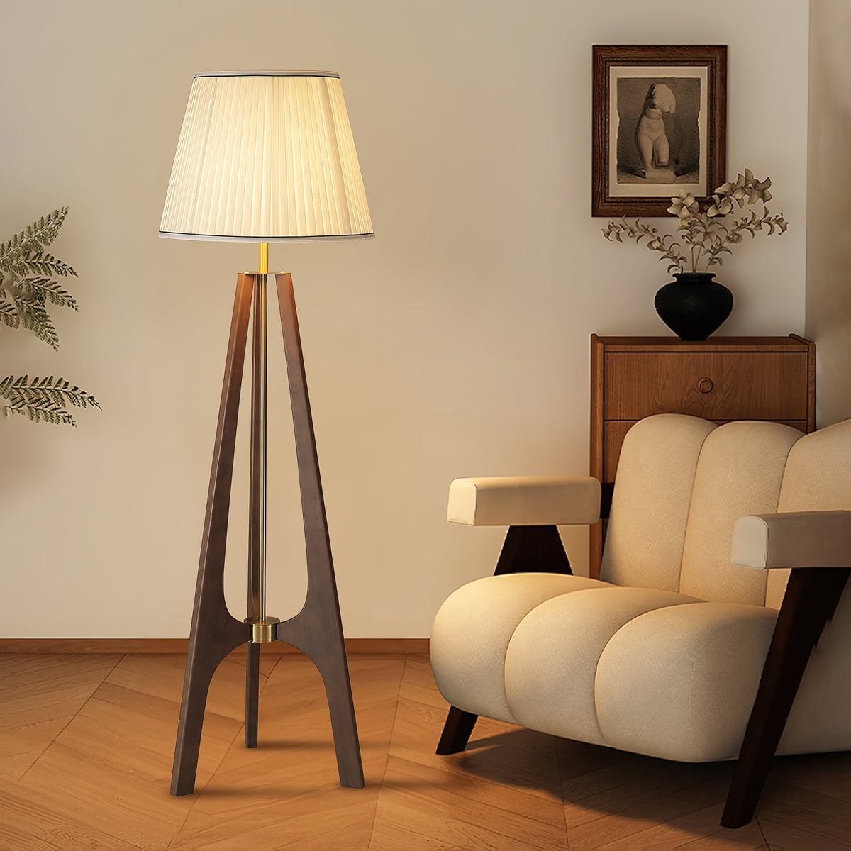Lámpara de pie trípode de madera con pantalla plisada blanca Sabina – junto a un sillón beige