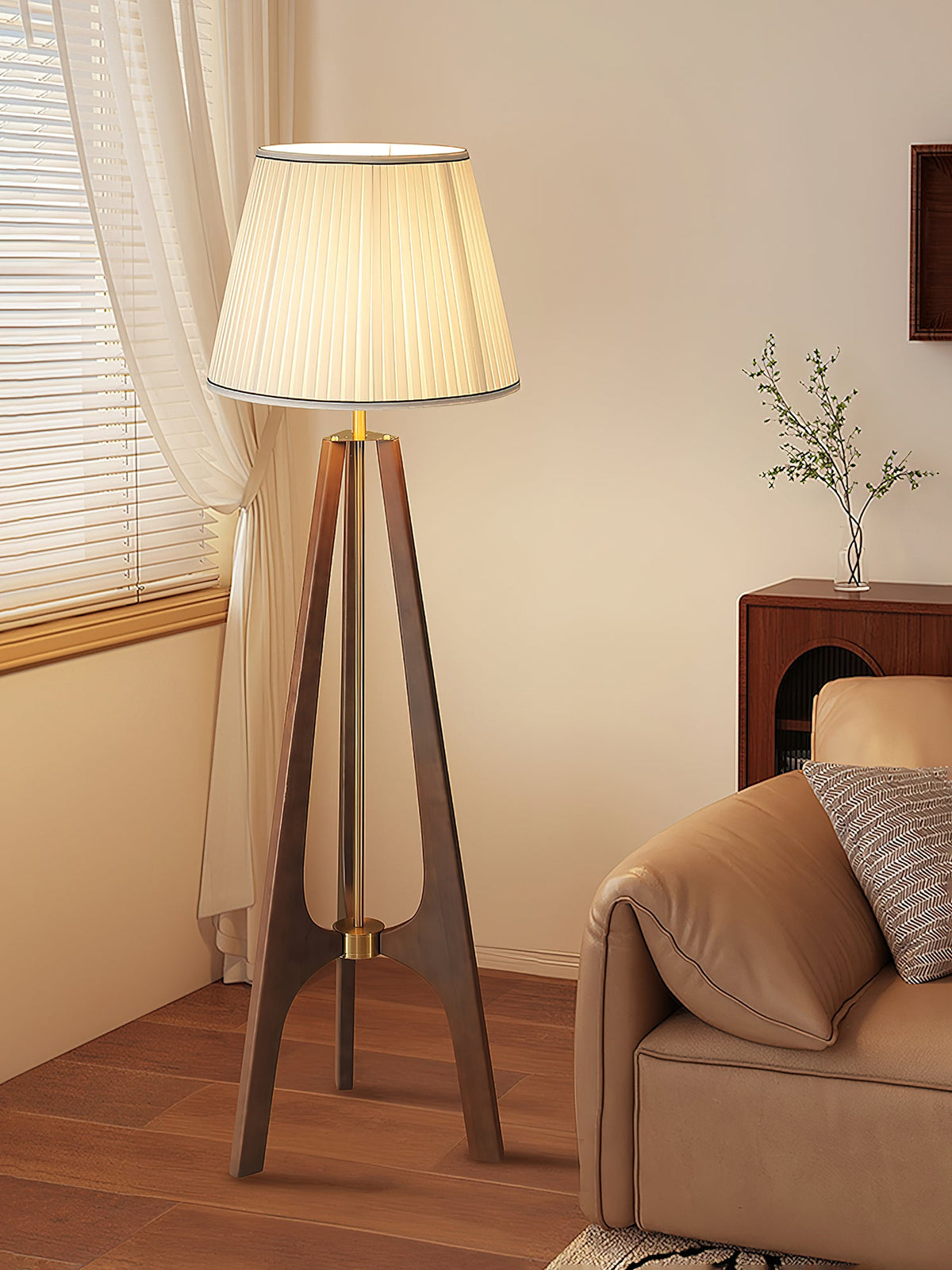 Lámpara de pie trípode de madera con pantalla plisada blanca Sabina – junto a un sofá marrón
