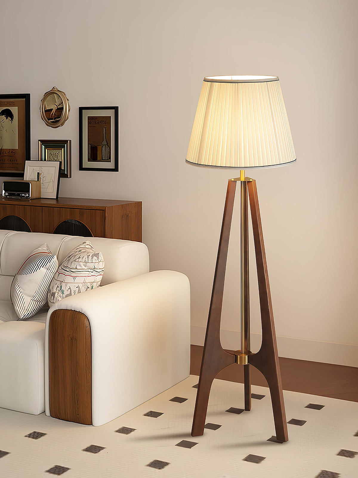 Lámpara de pie trípode de madera con pantalla plisada blanca Sabina – junto a un sofá claro con suelo de baldosas