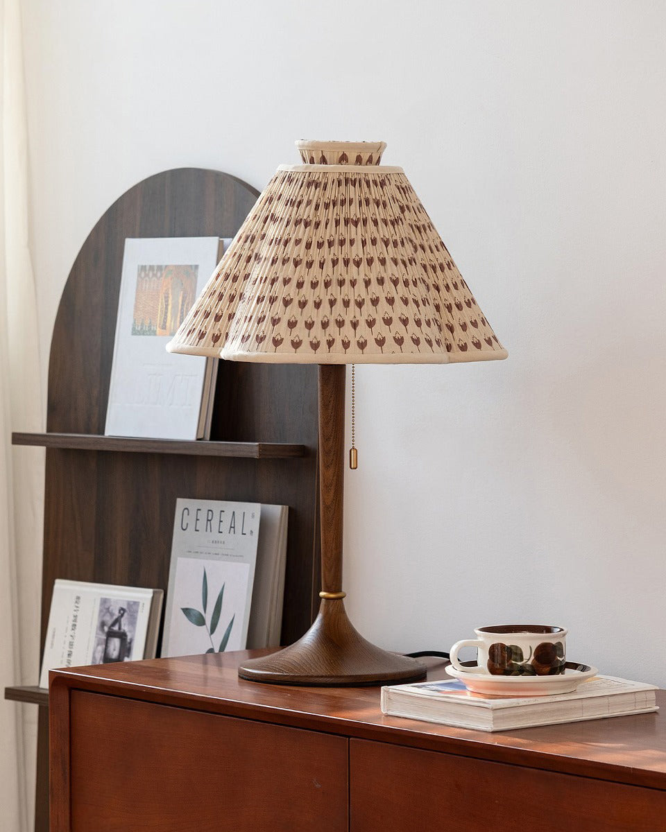 Lámpara de mesa plisada Tulipela – en una consola con libros