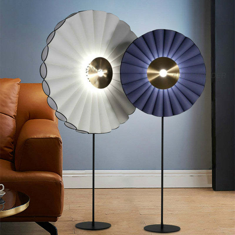 Lámpara de pie LED con disco plisado Zirena – blanca y azul junto a un sofá de cuero