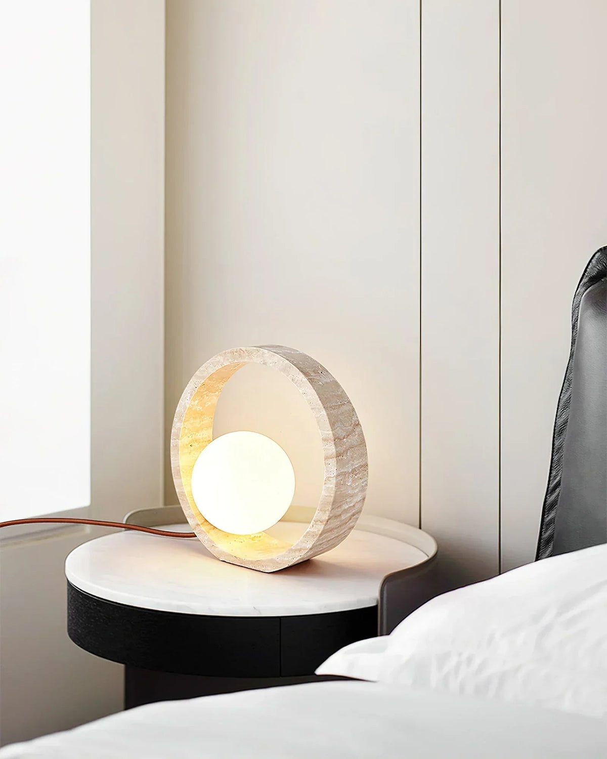 Lámpara de mesa de travertino Anella – junto a la cama sobre una mesita redonda