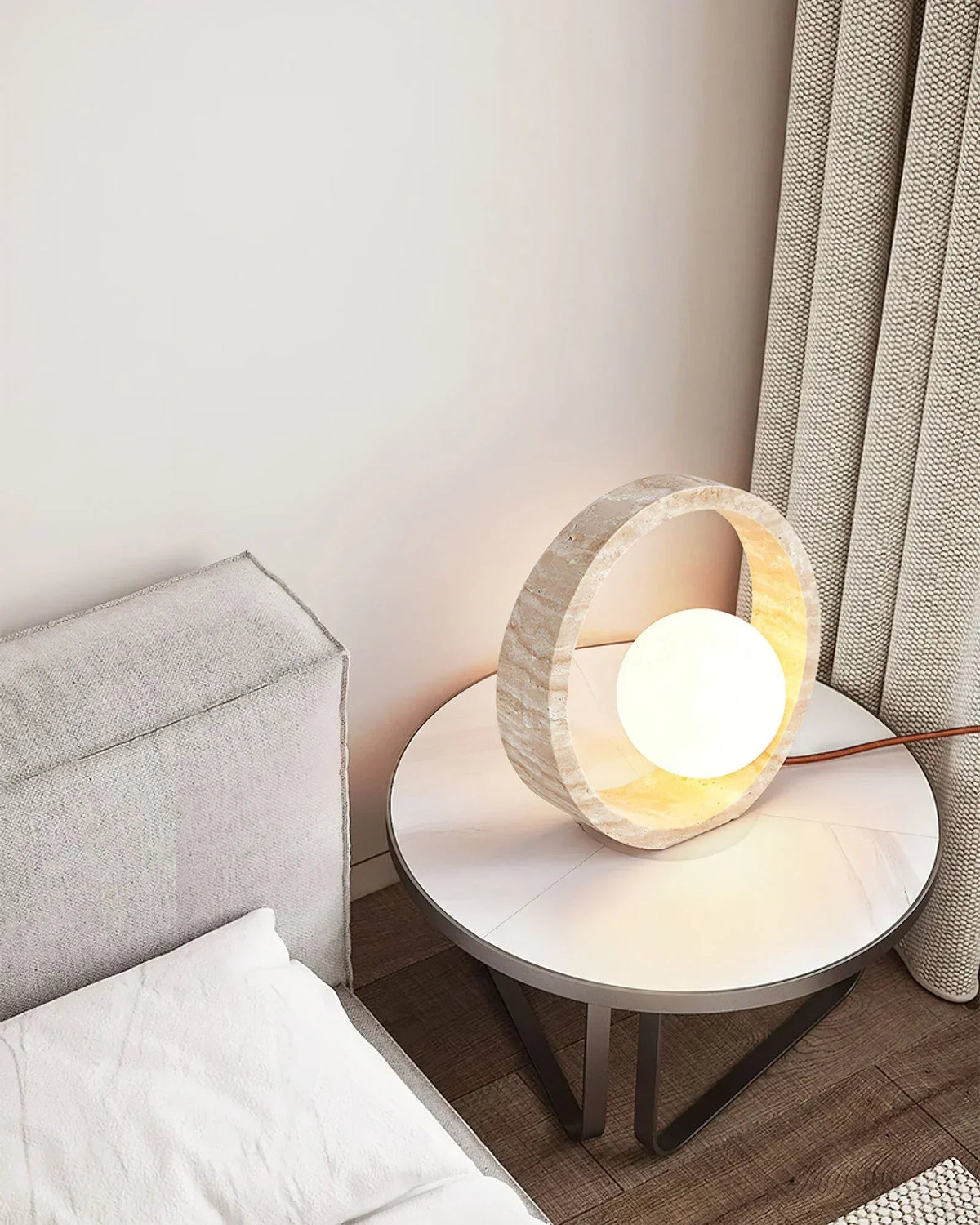 Lámpara de mesa de travertino Anella – en un dormitorio junto a un sofá gris