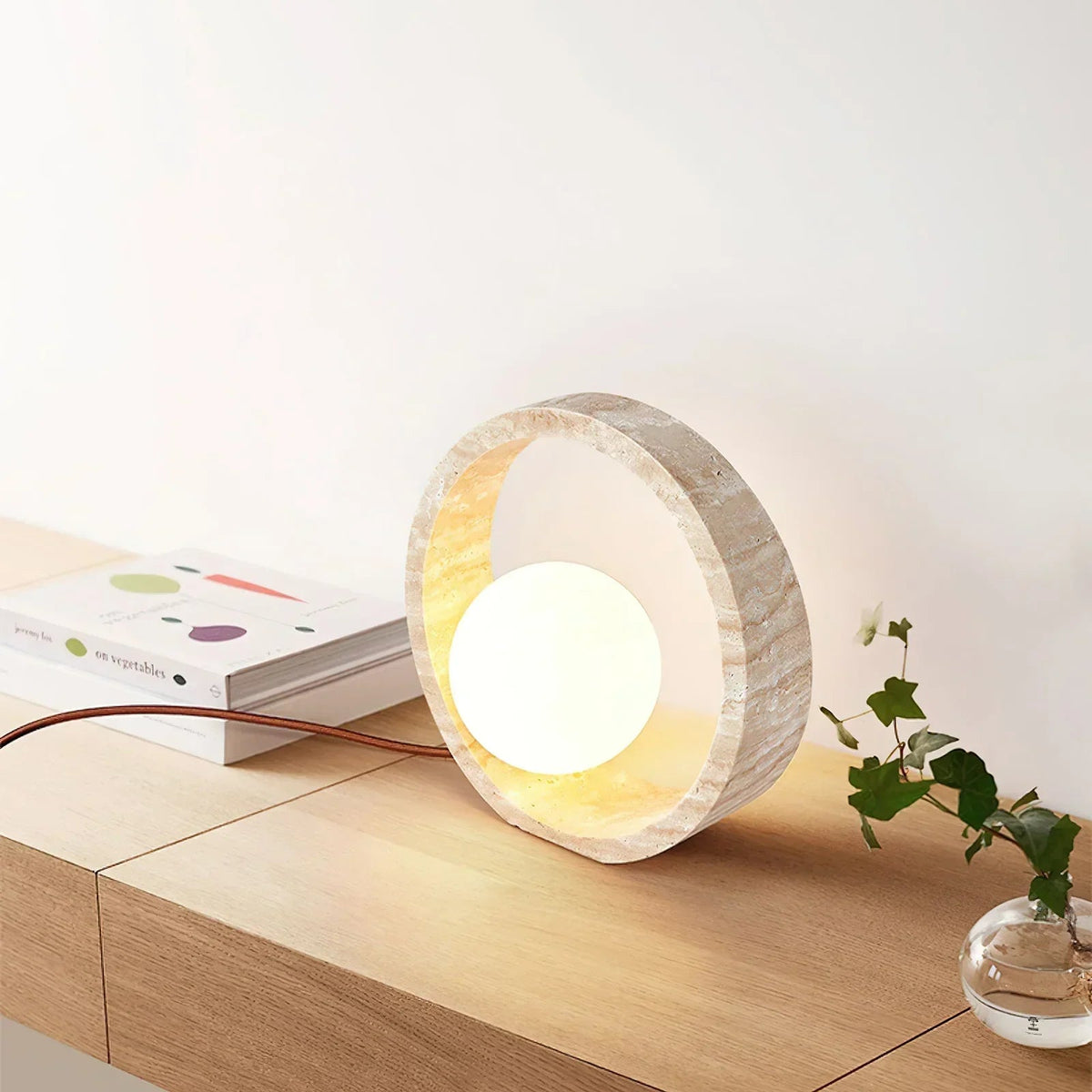 Lámpara de mesa de travertino Anella – sobre una mesita redonda junto a la cama