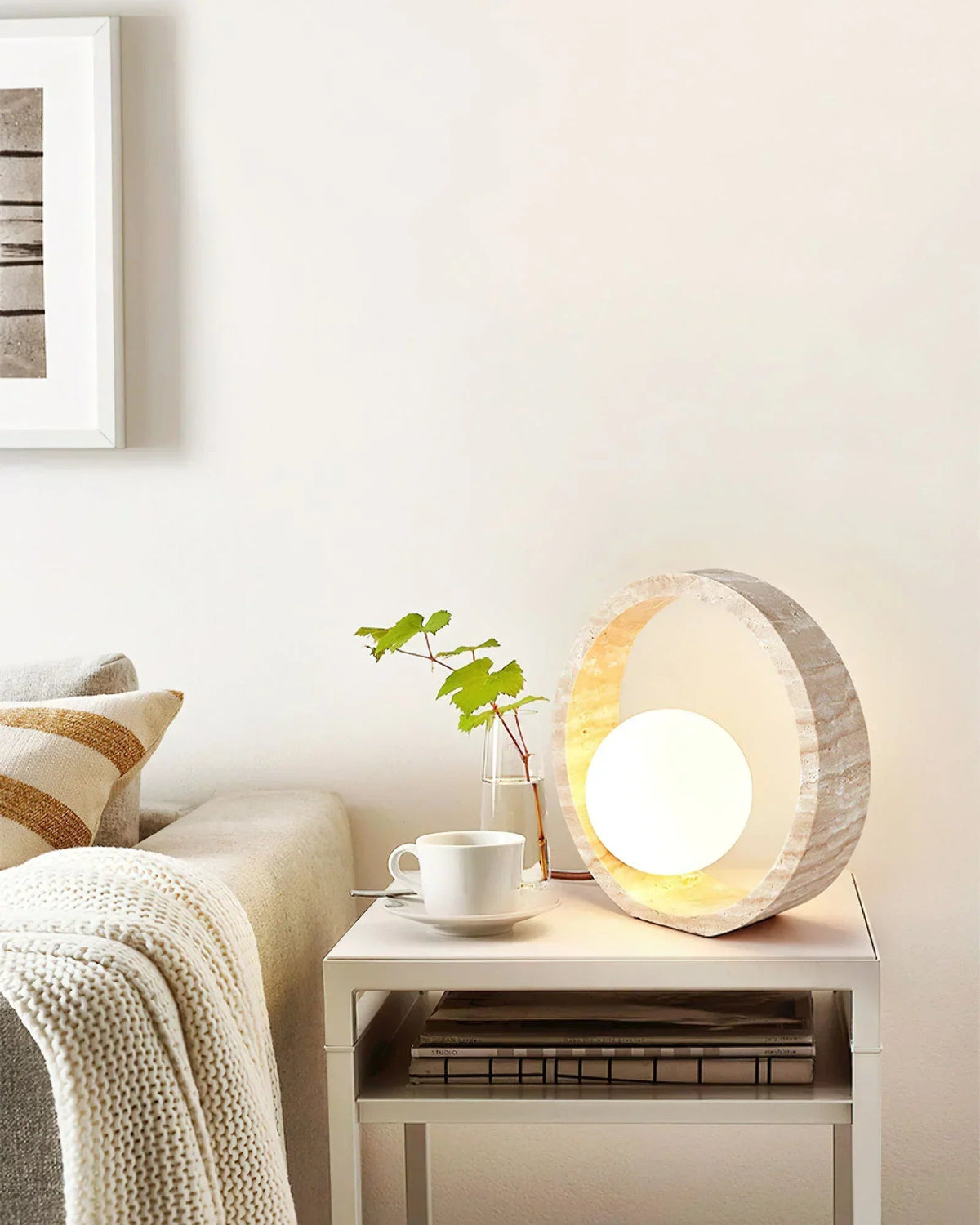 Lámpara de mesa de travertino Anella – encendida sobre un mueble de madera con un libro