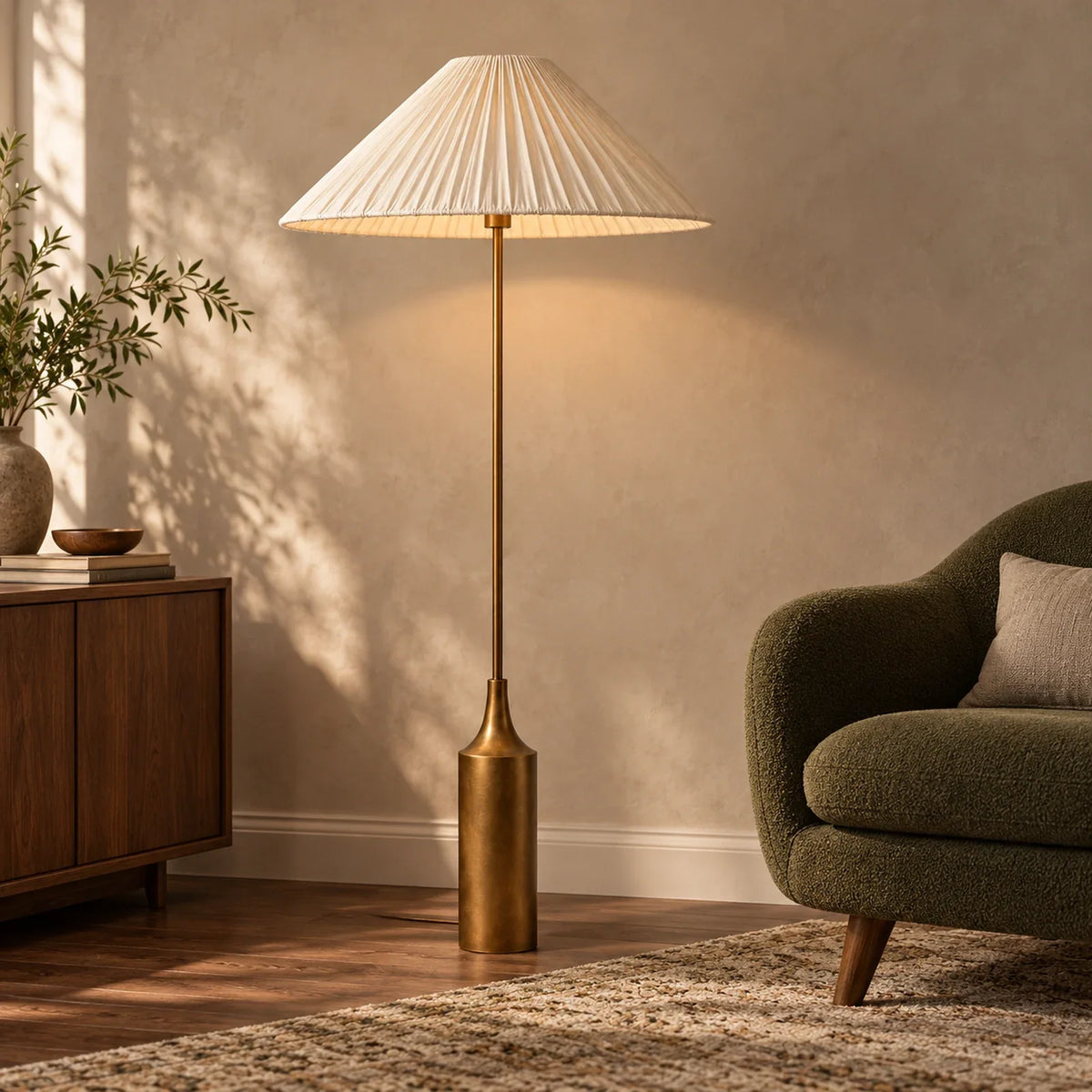 Lámpara de pie con pantalla plisada de lino y base latón Soleira – junto a un sillón verde oliva