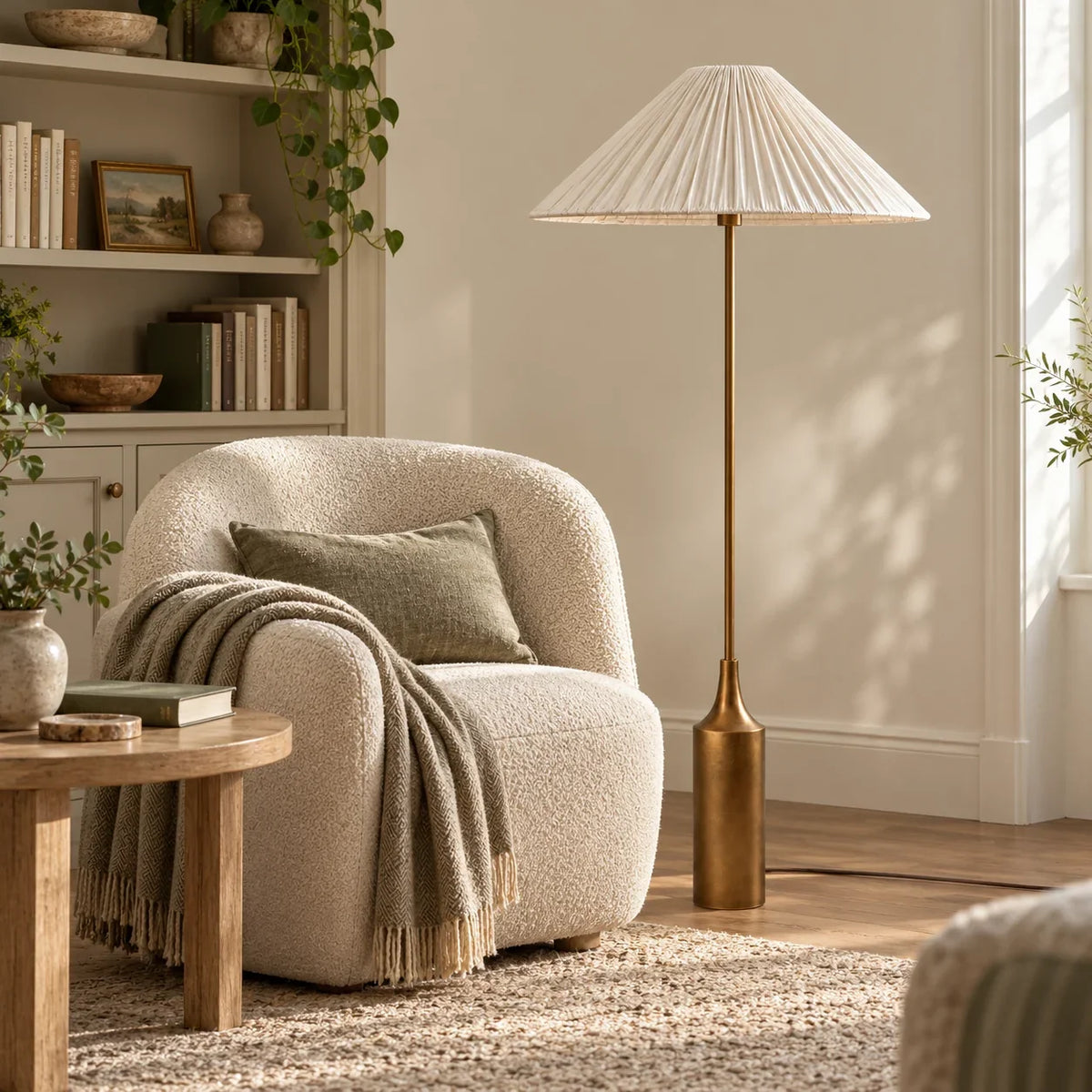 Lámpara de pie con pantalla plisada de lino y base latón Soleira – junto a un sillón de bouclé a la luz del día