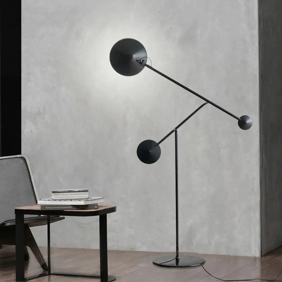 Lámpara de pie LED minimalista con brazos geométricos negros Cenvira – encendida junto a una pared de hormigón