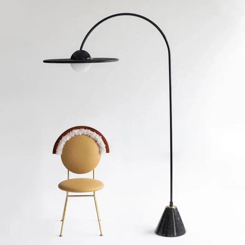 Lámpara de pie de arco negra con disco y globo de cristal Caldora – junto a una silla de diseño