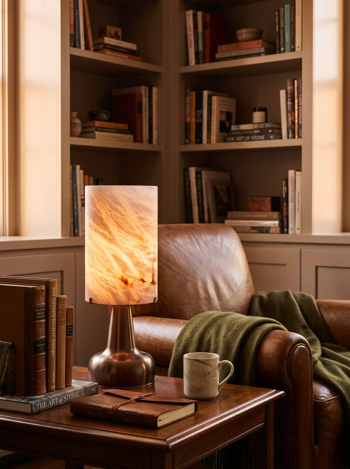 Lámpara de mesa de alabastro Merola – encendida junto a un sillón de cuero