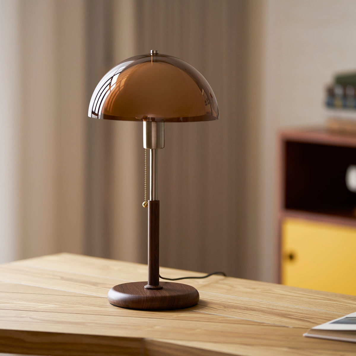 Lámpara de mesa retro Fambra – ámbar junto a un mueble de cajones de colores