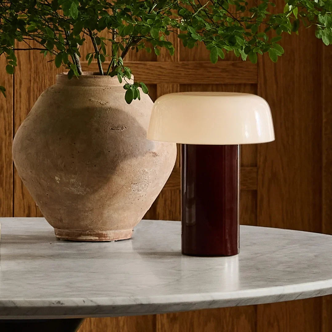 Lámpara de mesa seta de vidrio Feluna – versión grosella en una mesa de mármol con jarrón
