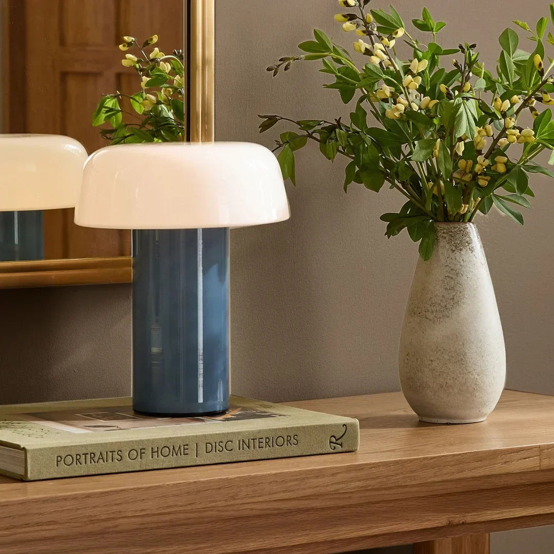 Lámpara de mesa seta de vidrio Feluna – versión pizarra sobre libros en un aparador con flores