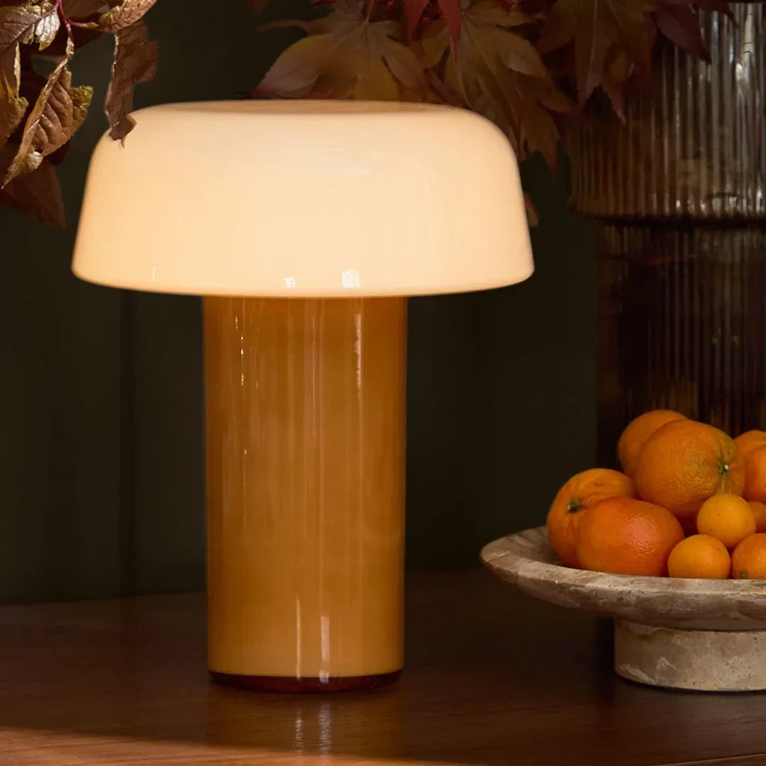 Lámpara de mesa seta de vidrio Feluna – versión ámbar encendida junto a un frutero