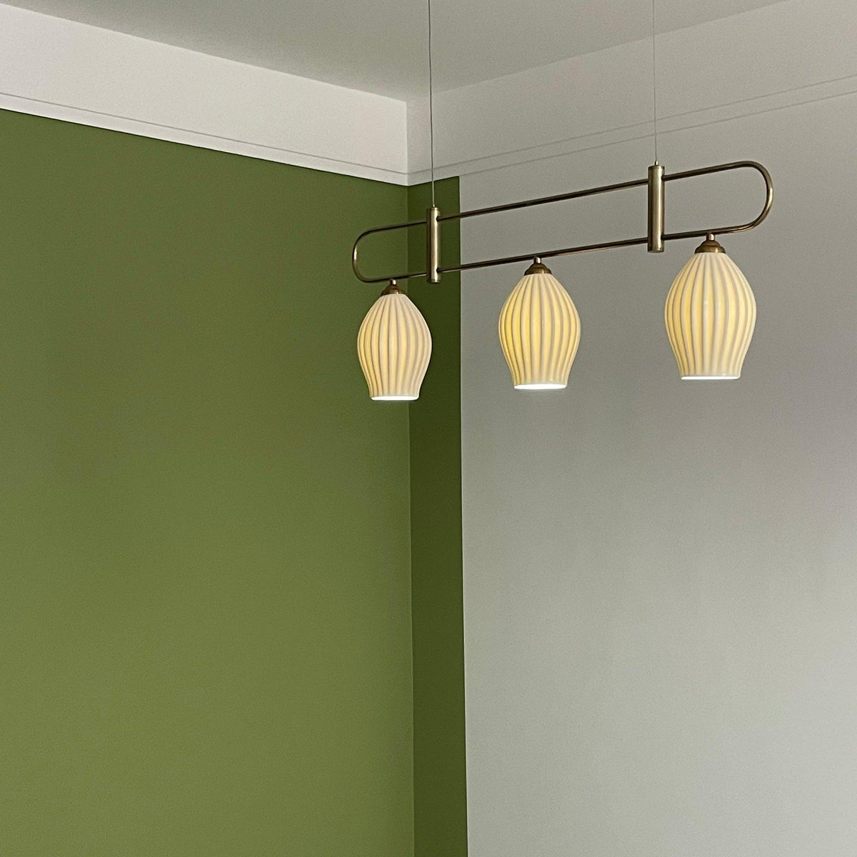 Lámpara colgante lineal de cerámica Gajela – níquel de tres luces en una pared verde