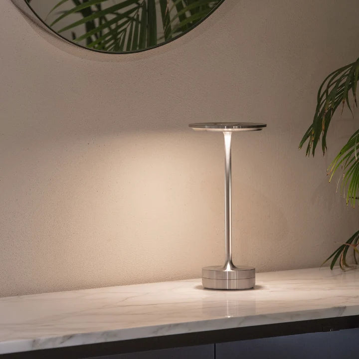 Lámpara de mesa portátil Raliza – versión plateada en un baño con espejo redondo