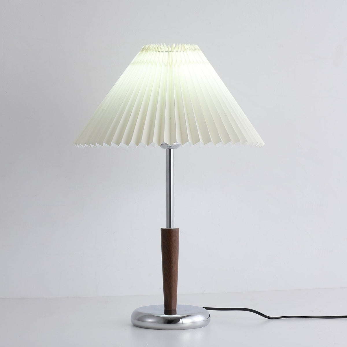 Lámpara de mesa con pantalla plisada Ivenna – encendida junto a una butaca