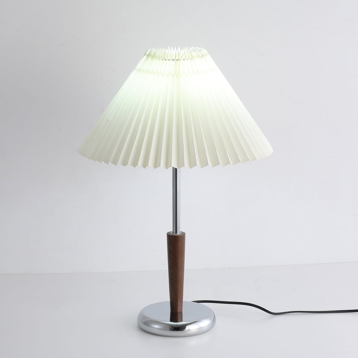 Lámpara de mesa con pantalla plisada Ivenna – encendida en una mesita junto a un sofá