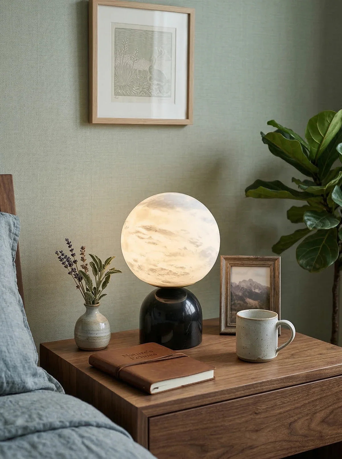Lámpara de mesa de alabastro Kelaria – encendida sobre una mesita de noche con plantas