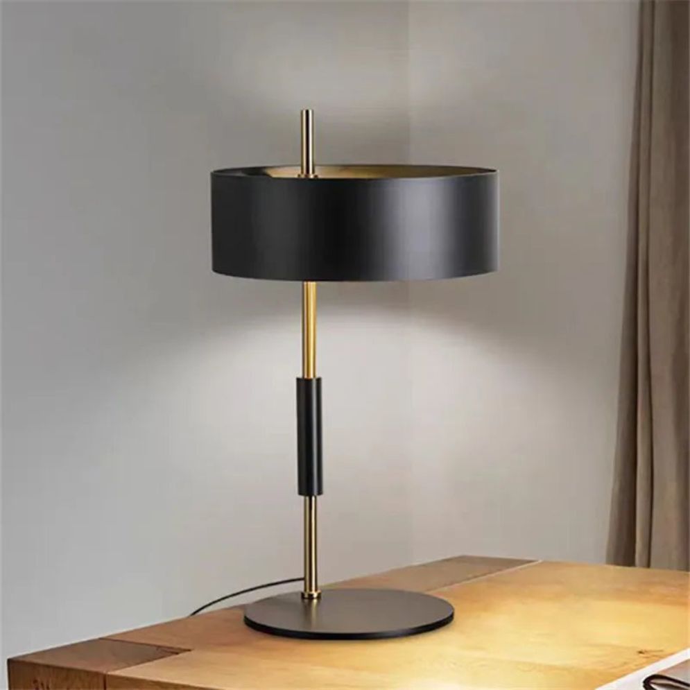 Lámpara negra y dorada Vandela – versión de mesa sobre un mueble de madera