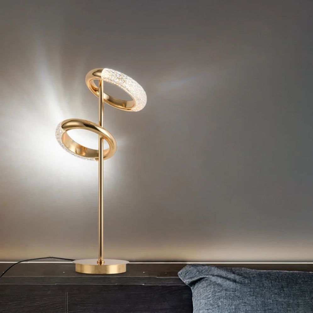 Lámpara de pie LED con anillos dorados Sortiva – versión de mesa encendida sobre un mueble