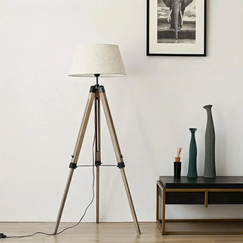 Lámpara de pie trípode de madera Simarel – con pantalla blanca junto a un mueble