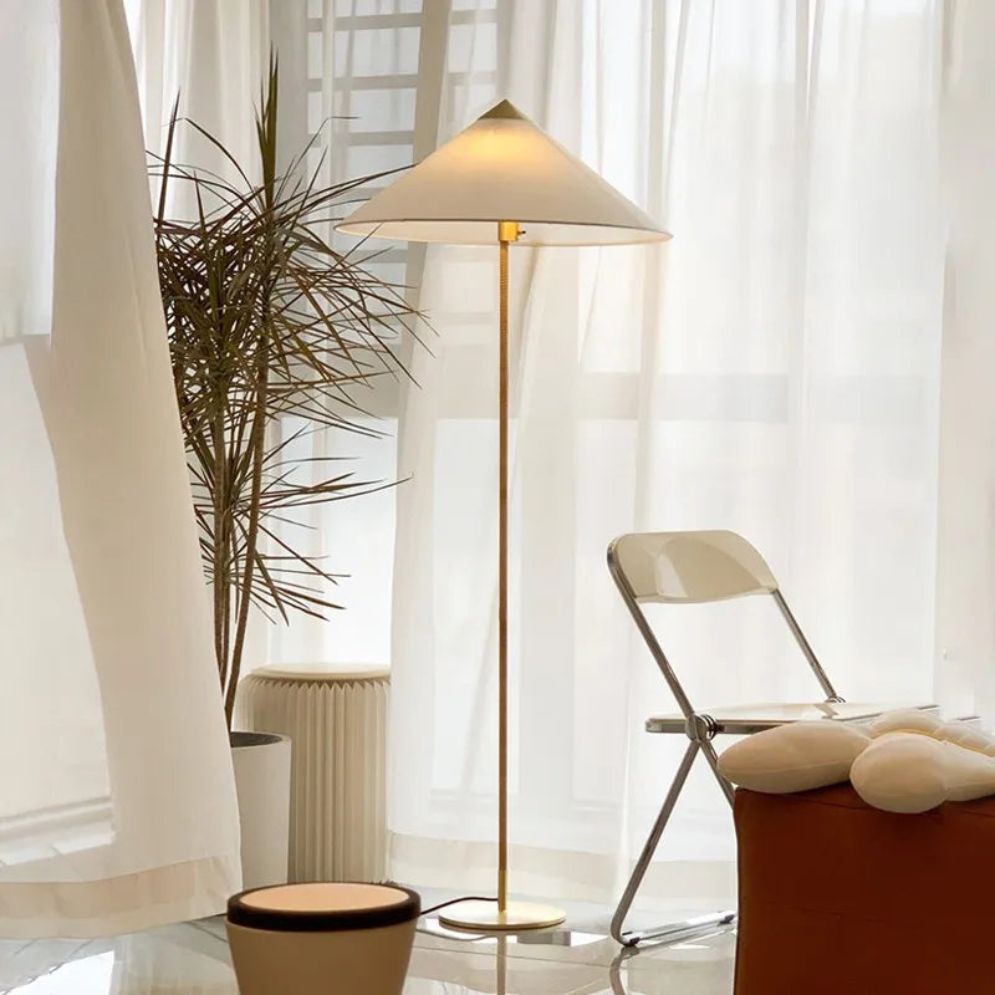 Lámpara de pie con pantalla cónica Bacora – de tela blanca junto a una ventana