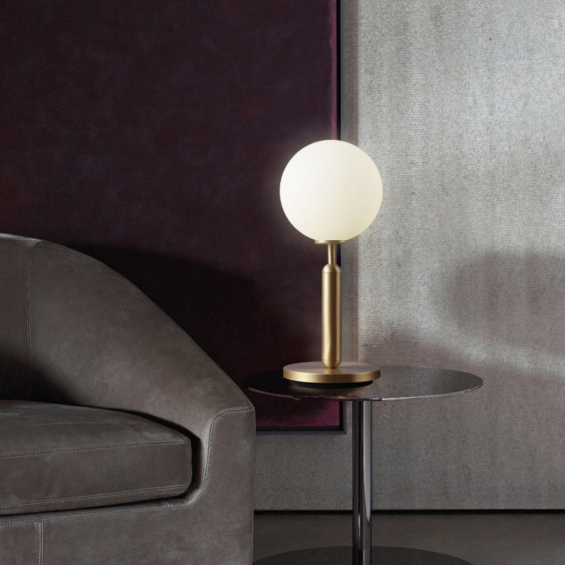 Lámpara de mesa globo Sferla – encendida junto a un sillón de piel