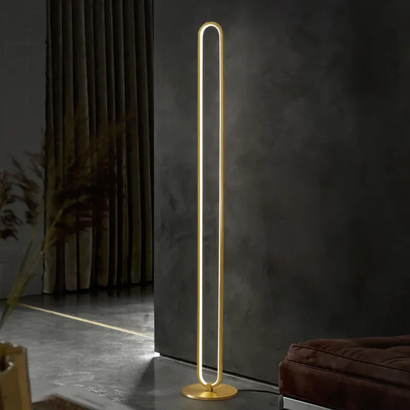 Lámpara de pie LED lineal de latón Yunela – encendida junto a una pared oscura