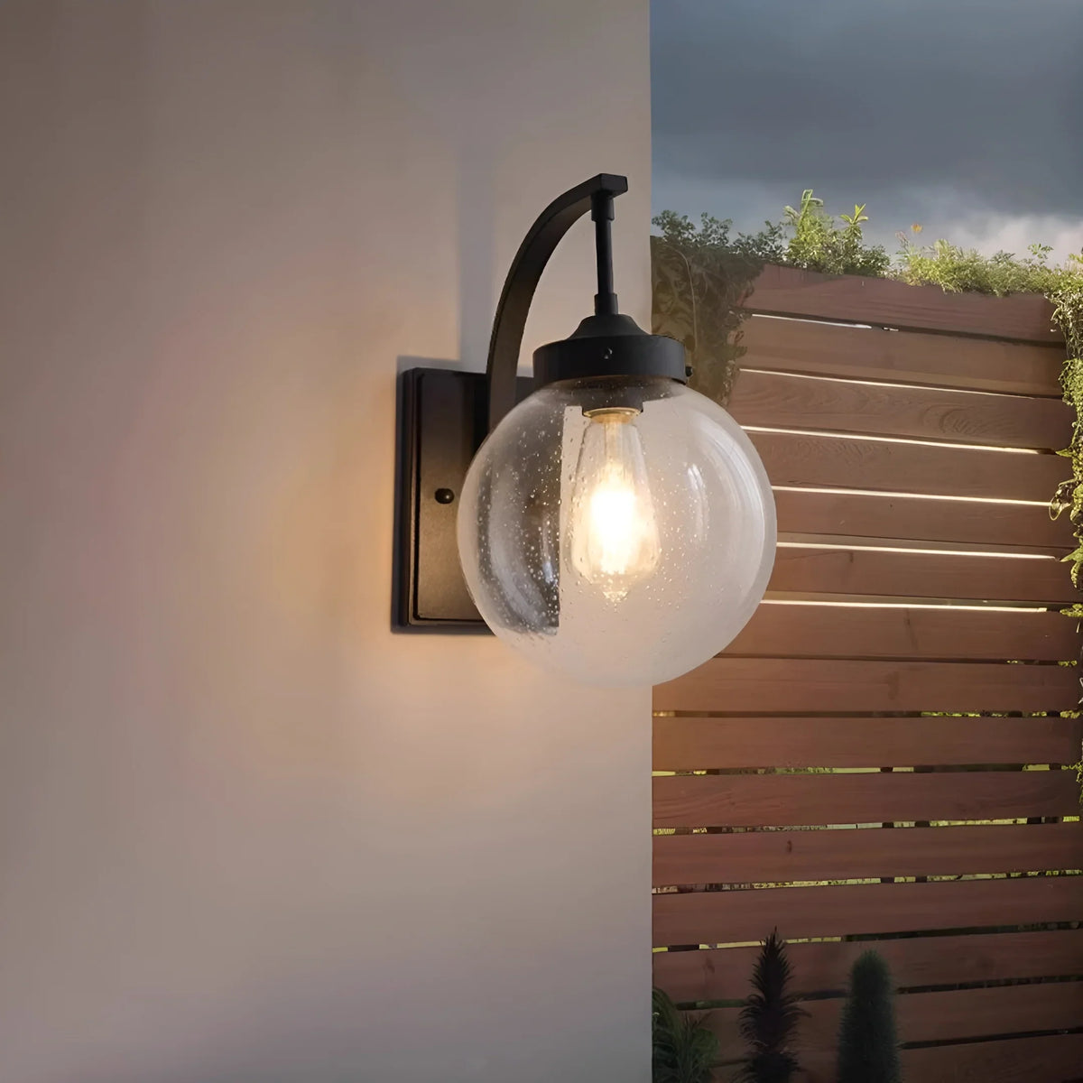 Aplique de pared exterior Ozela – en negro junto a una valla de madera