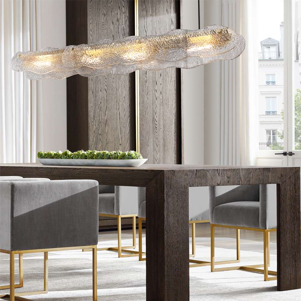 Lámpara colgante lineal de cristal ondulado Brumara – sobre una mesa de madera oscura