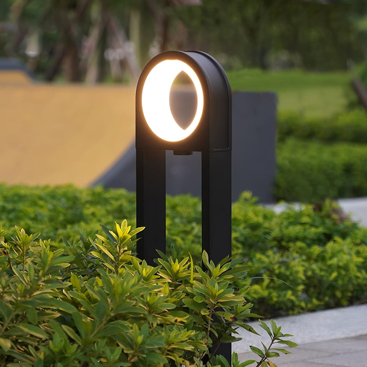 Baliza de jardín LED Oliano – remate redondo encendido junto a un seto