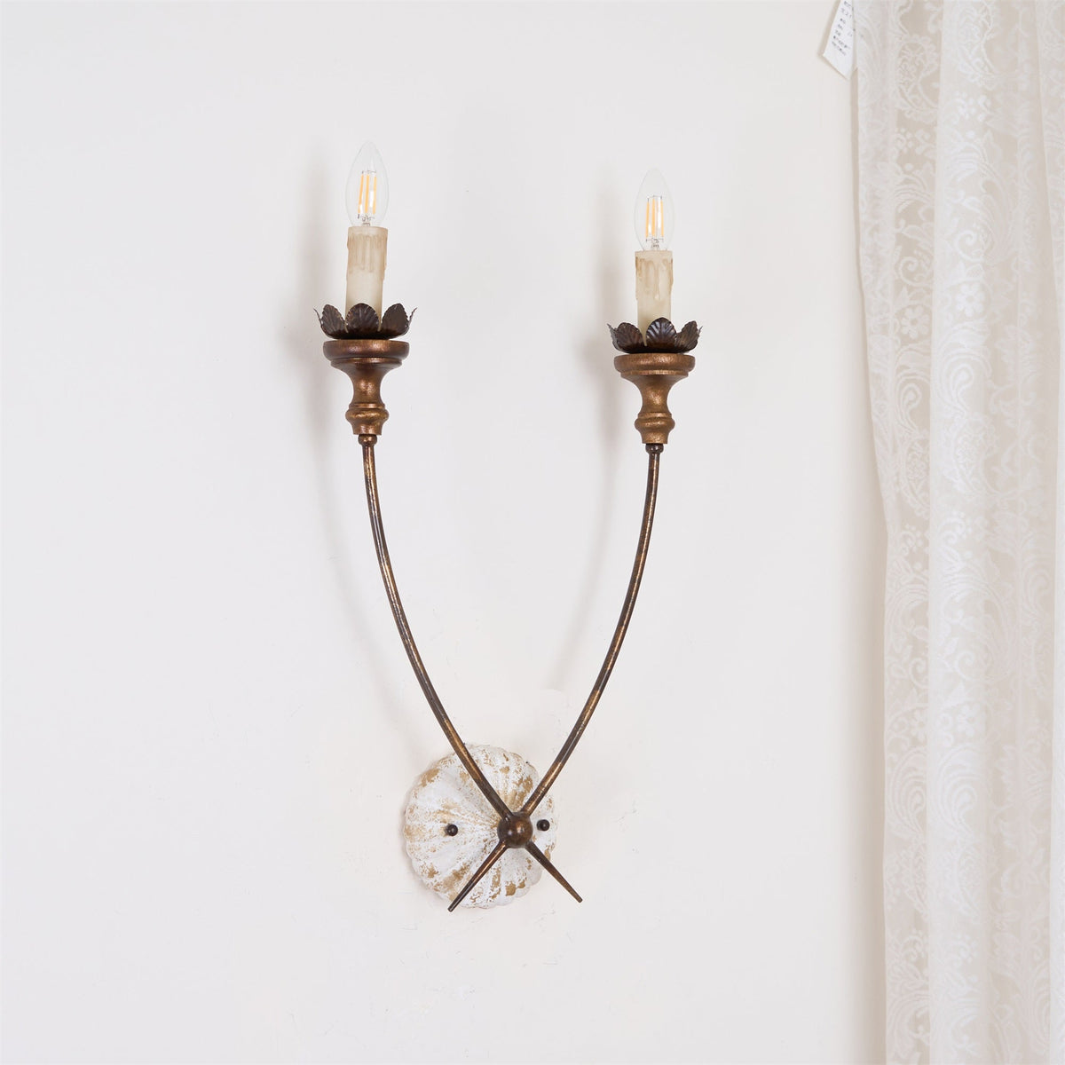 Aplique de pared vintage de dos velas Oscela – encendido sobre una pared blanca