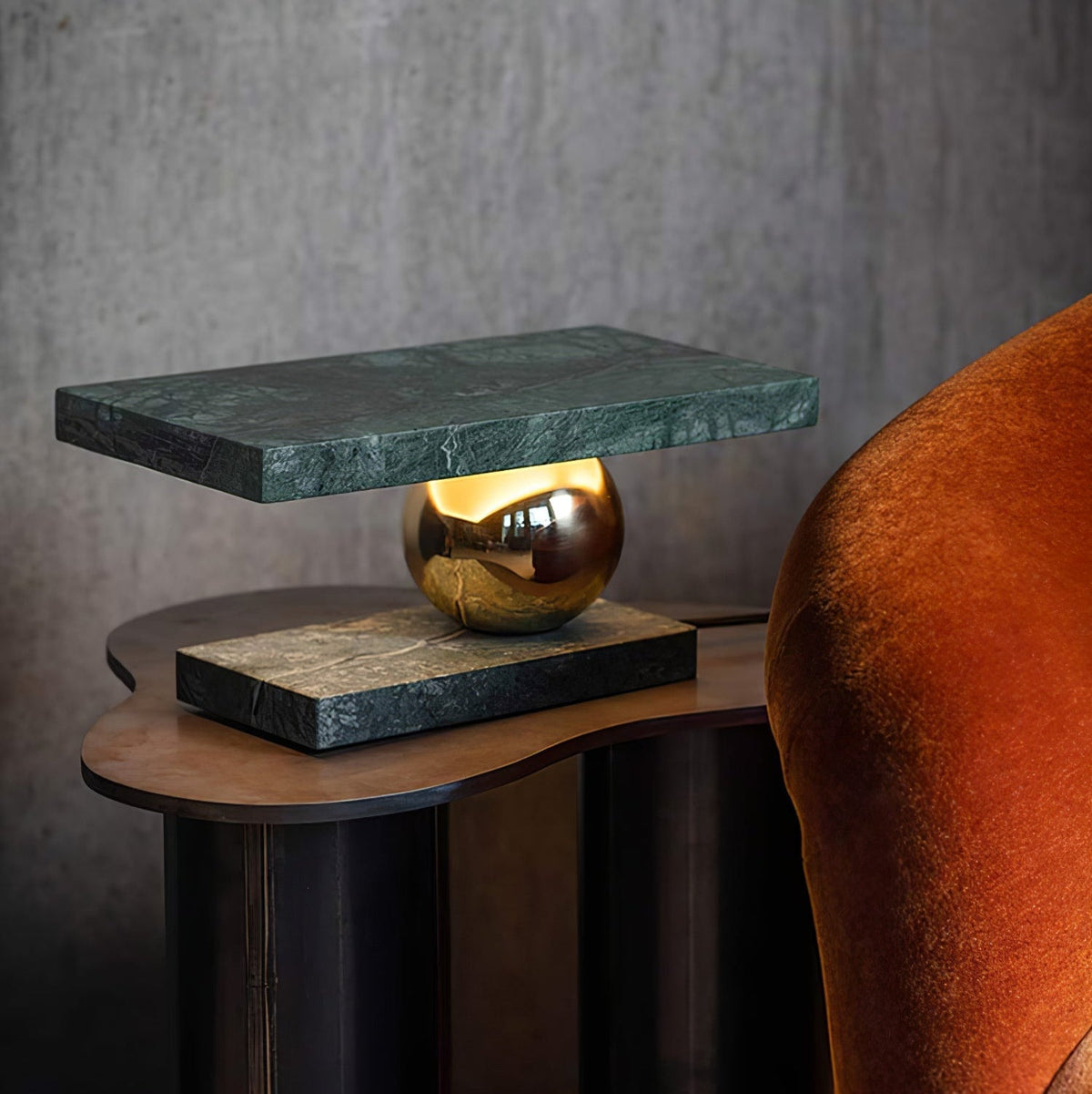 Lámpara de mesa de mármol Quasara – versión en mármol verde encendida junto a un sofá de terciopelo