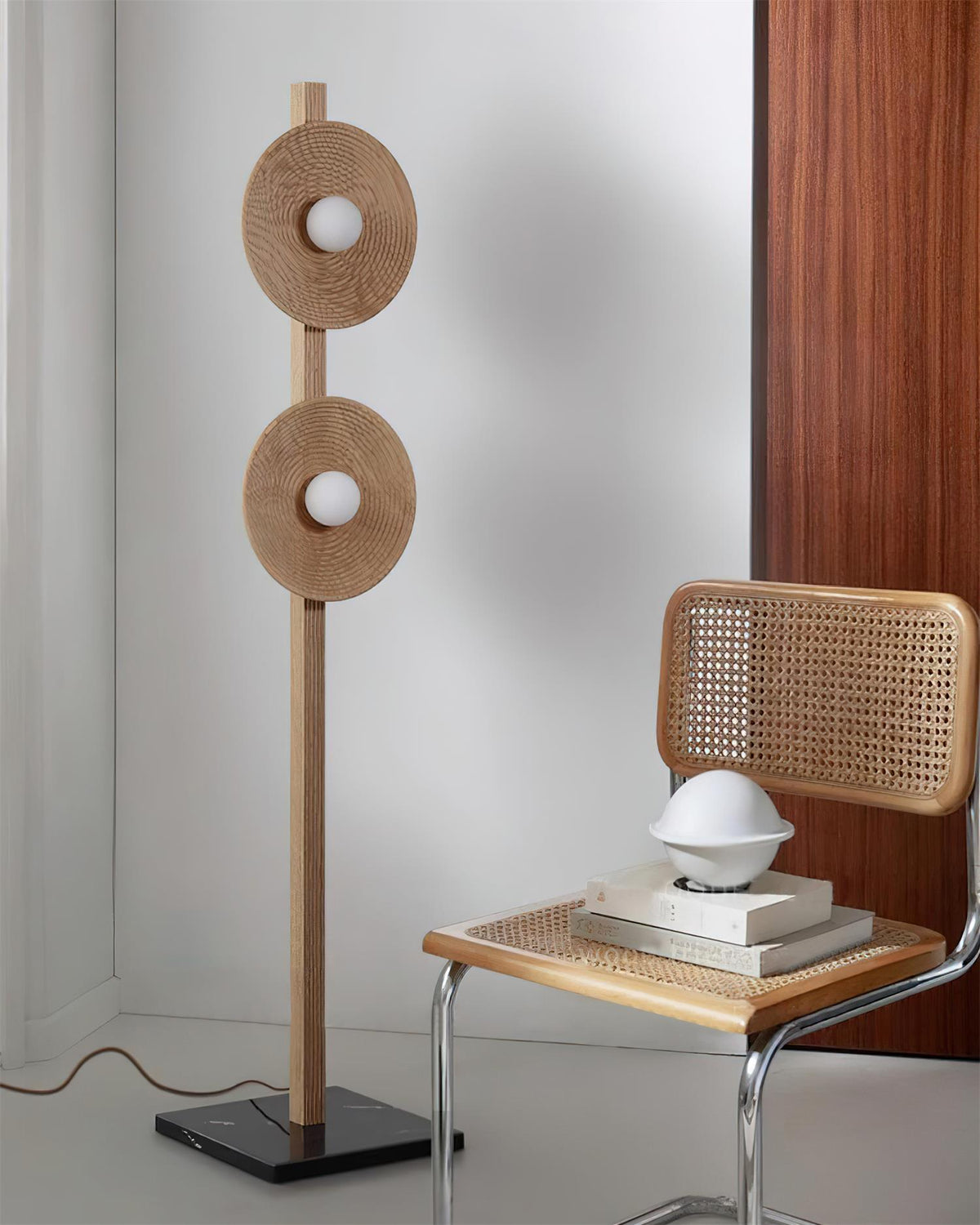 Lámpara de pie de madera con dos discos Radeva – madera natural junto a una silla de rejilla