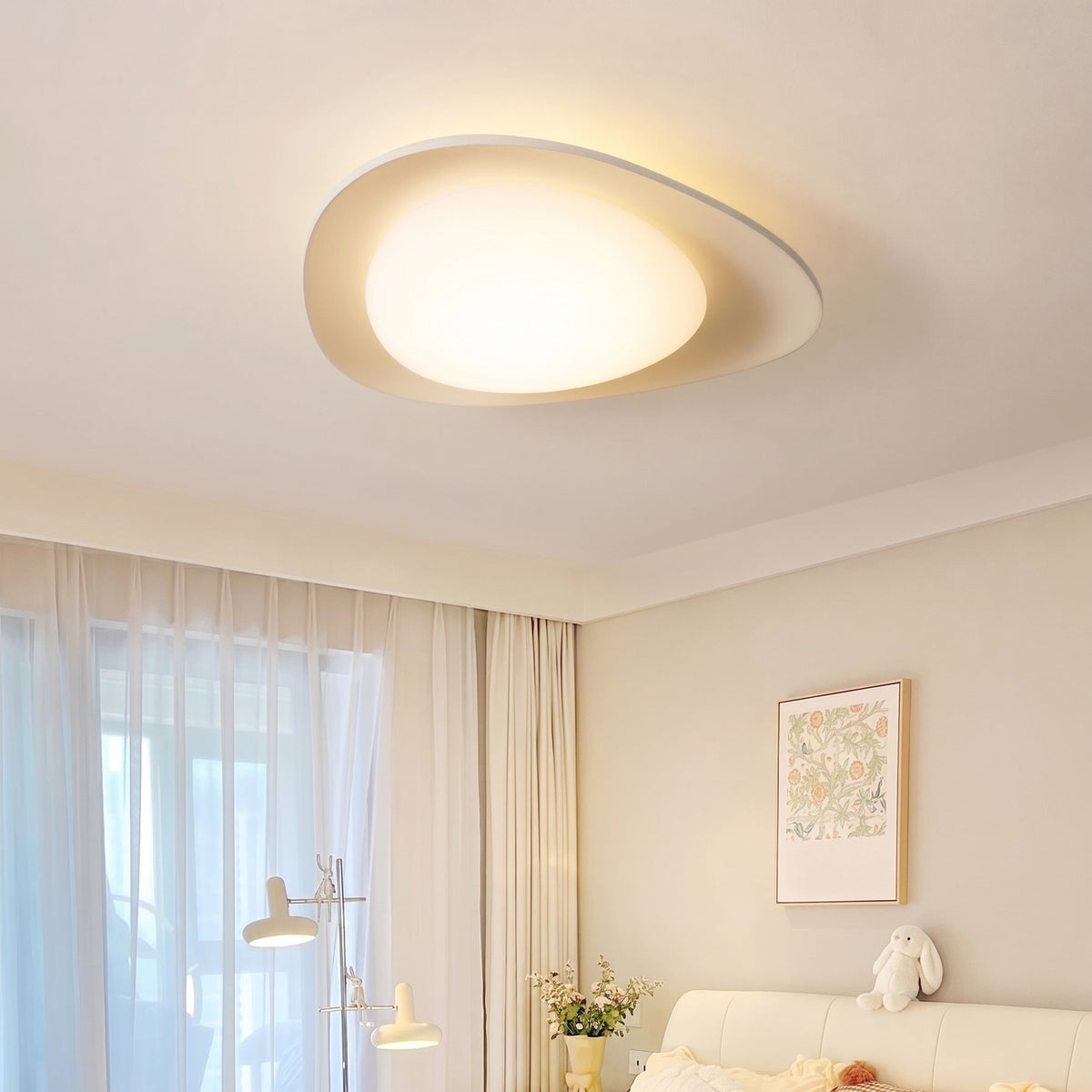 Plafón LED en forma de canto rodado Cantela – en un dormitorio con cortinas blancas