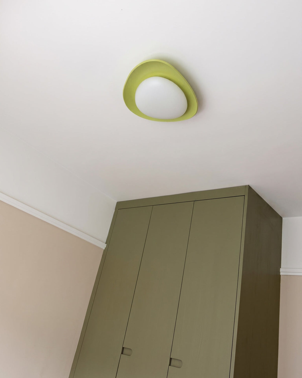 Plafón LED en forma de canto rodado Cantela – con aro verde sobre un armario
