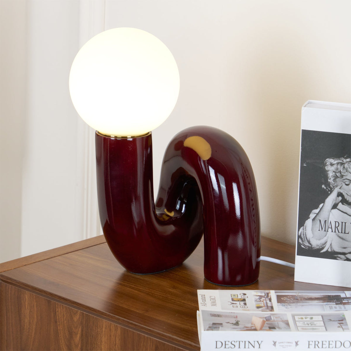 Lámpara de mesa escultural Rizeta – burdeos encendida junto a unos libros
