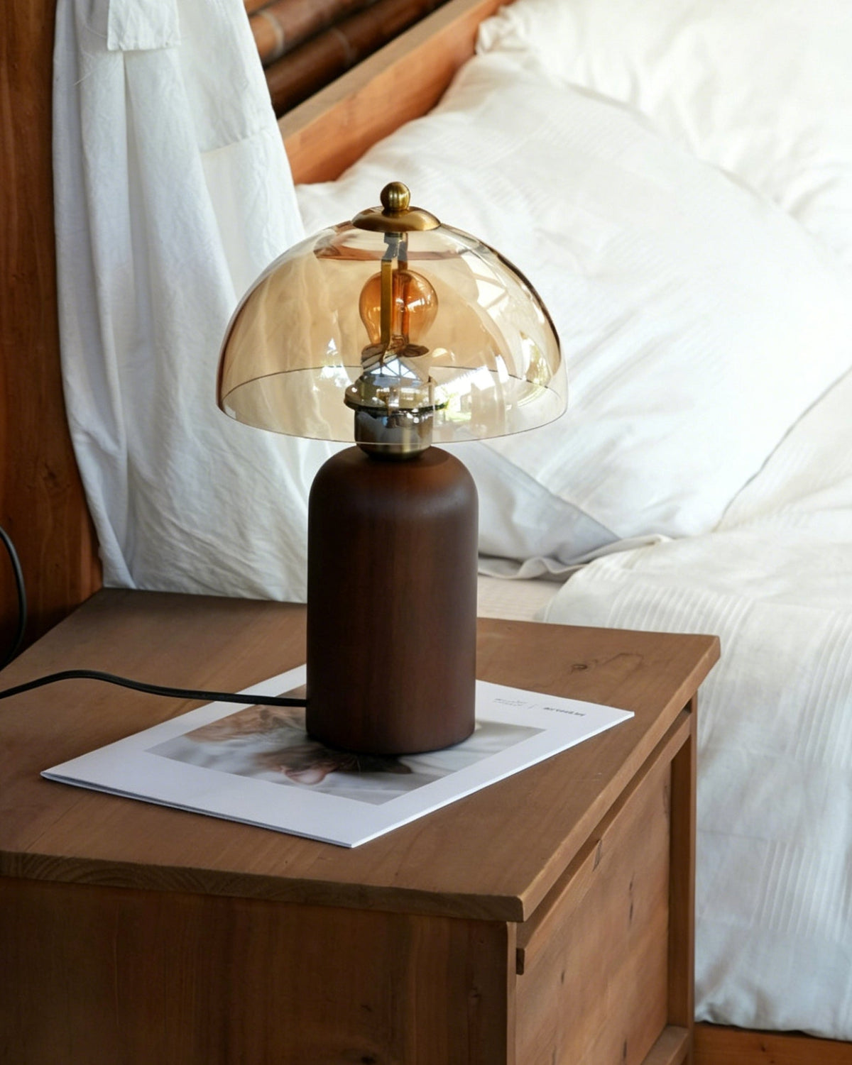 Lámpara de mesa de madera y cristal ámbar Rubana – encendida sobre una mesilla junto a la cama