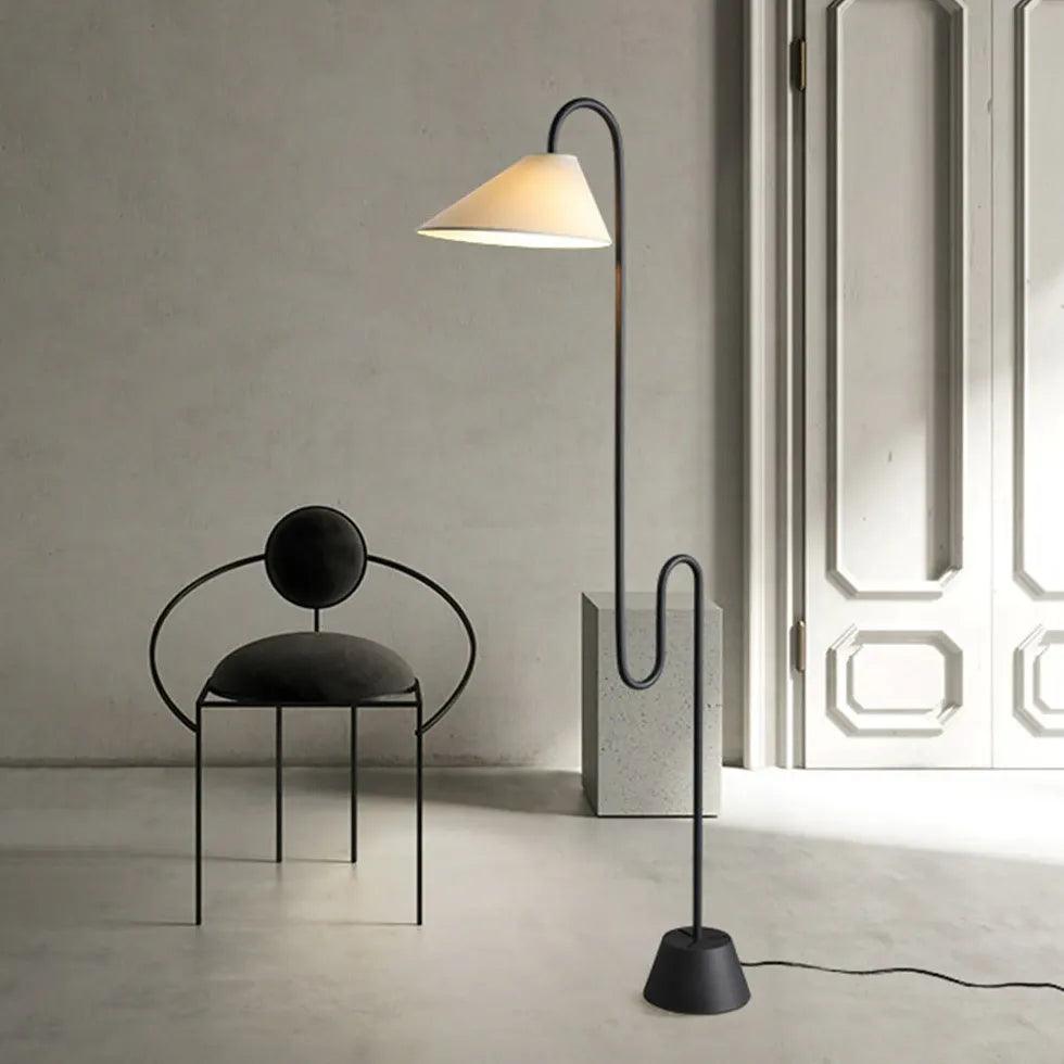 Lámpara de pie curva Idalia – junto a una silla negra de diseño en un salón con paredes claras