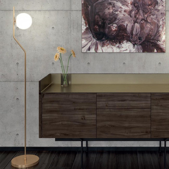 Lámpara de pie minimalista Saluna con esfera de cristal – tallo dorado junto a un aparador
