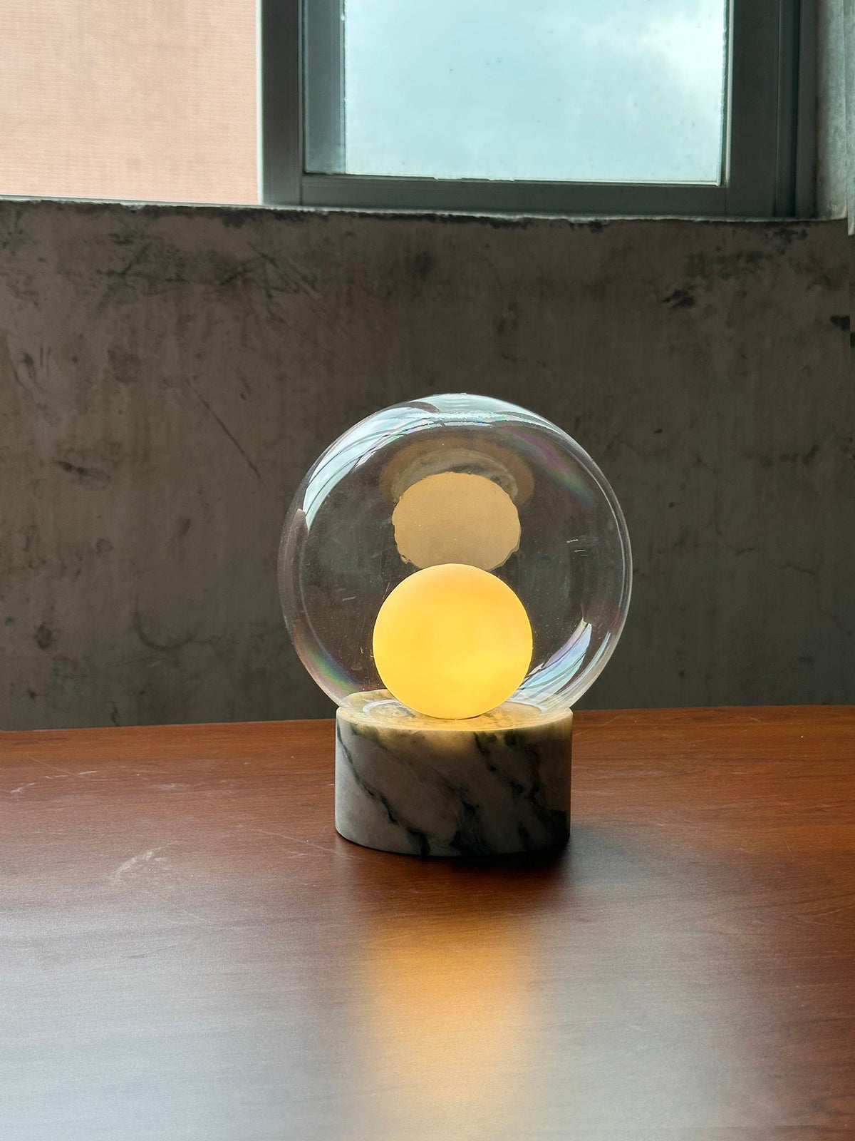 Lámpara de mesa de cristal Saquira – encendida sobre una mesa de madera