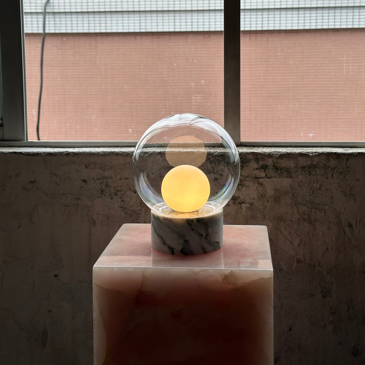 Lámpara de mesa de cristal Saquira – encendida sobre un pedestal