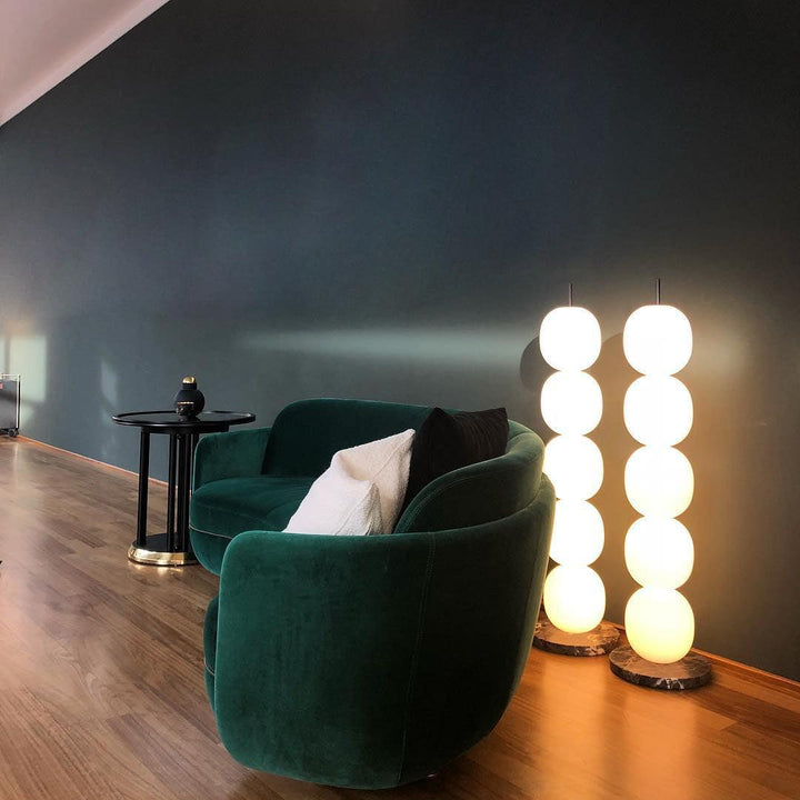 Lámpara de pie de esferas de vidrio opal Sartina – encendida junto a un sillón de terciopelo