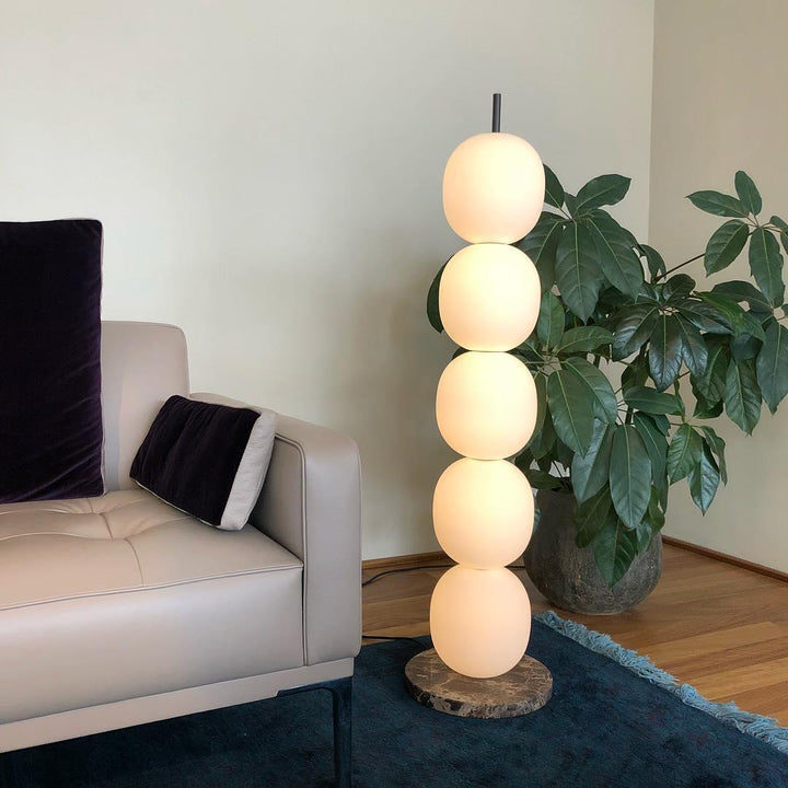 Lámpara de pie de esferas de vidrio opal Sartina – encendida junto a un sofá