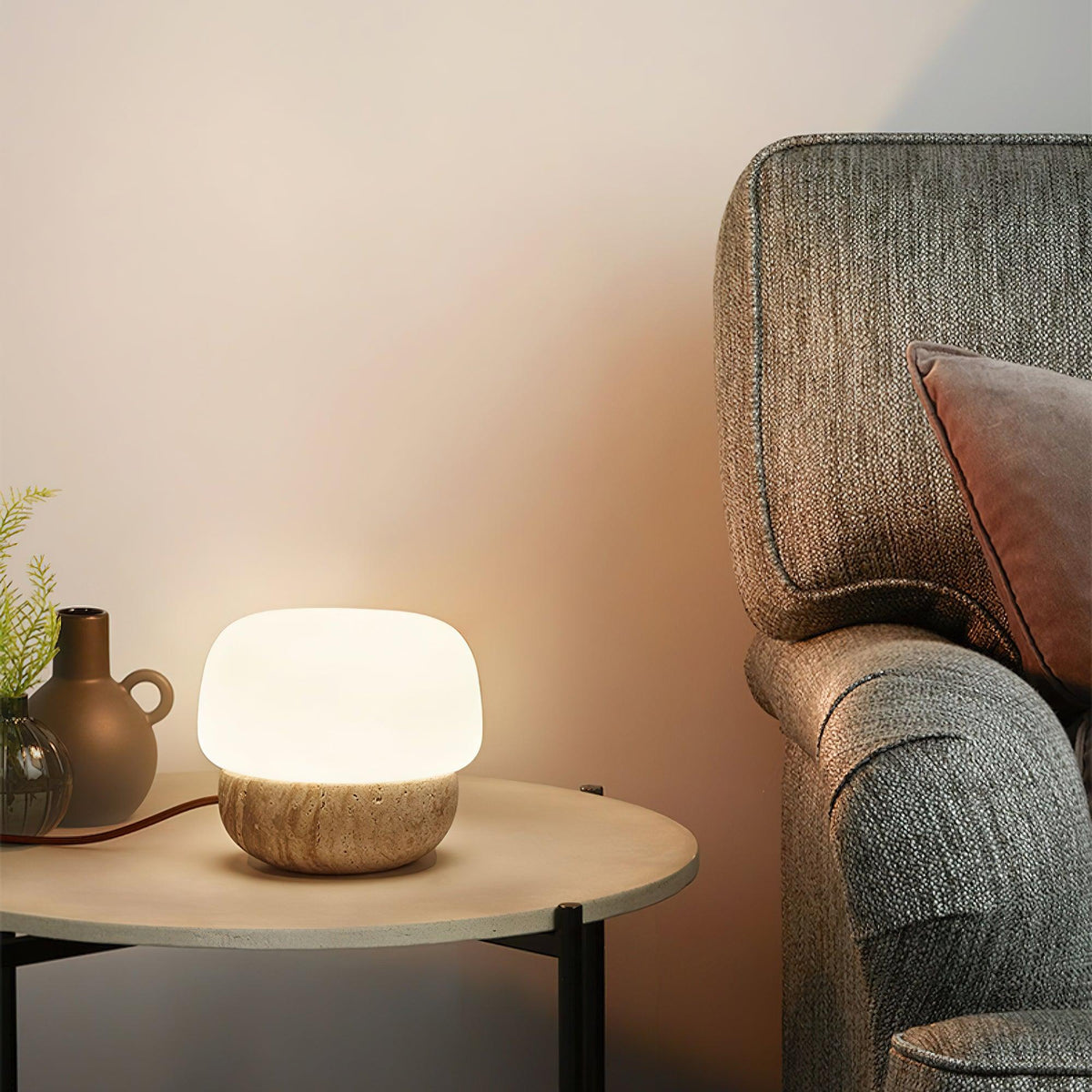 Lámpara de mesa de travertino Setina – en una mesa auxiliar junto a un sillón