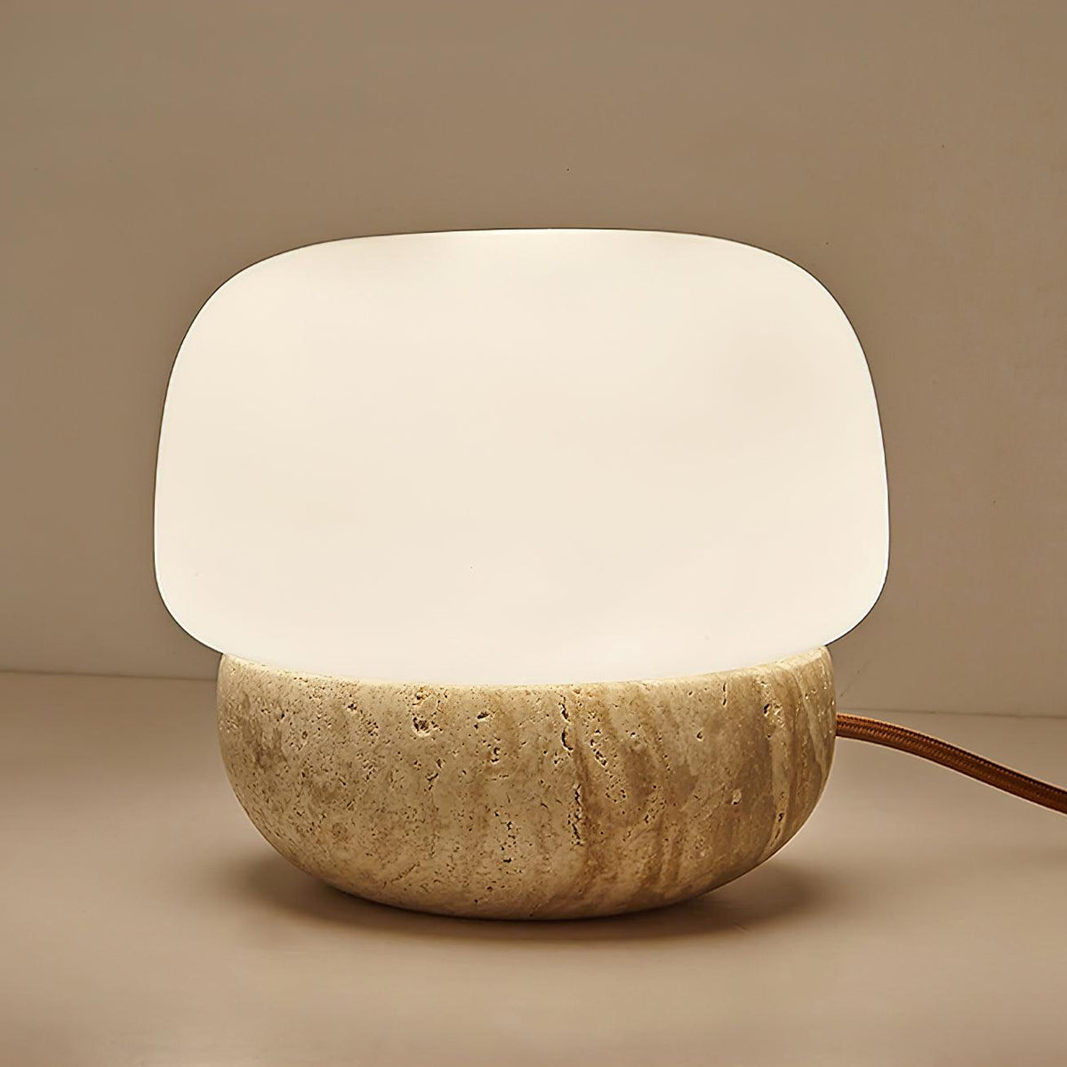 Lámpara de mesa de travertino Setina – encendida sobre fondo cálido