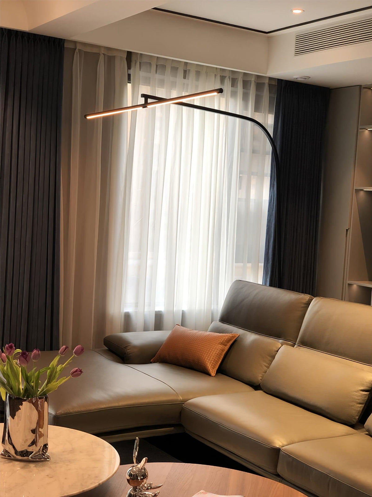 Lámpara de pie de arco LED Sigela – sobre un sofá de piel gris